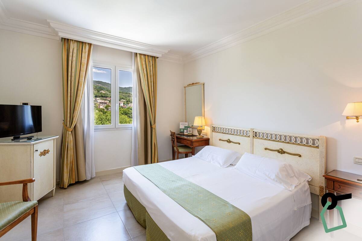 Une chambre d’hôtel avec un lit, une télévision, un bureau avec une lampe et une vue sur la verdure.