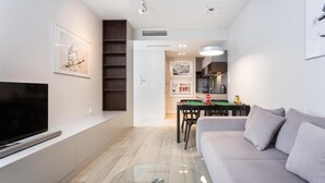 A modern living room with a flat-screen TV, a glass coffee table, a grey sofa, and a dining area with a table and chairs. - 1-bedroom in city center | balcony | close to the Main Square and Jewish Quarter (Kraków)