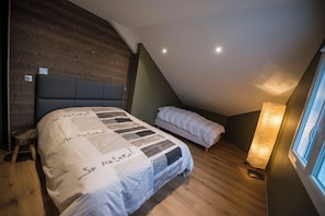 A bedroom with a sloped ceiling, a bed with a quilt, a bedside table, and a lamp.