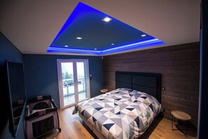 A bedroom with a geometric-patterned bedspread, a wooden headboard, and a ceiling with blue LED lighting.