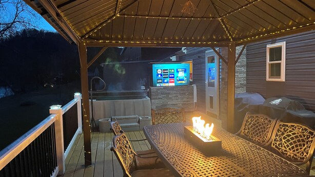 En utomhusveranda med ett takförsett sittområde, en bubbelpool och en tv-skärm som visar olika kanaler.