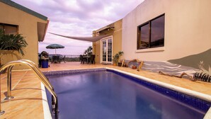 Una piscina con un toldo, un patio con mobiliario exterior y vista al cielo.