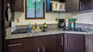 Una cocina con encimeras de granito, armarios de madera oscura, microondas, cafetera y ventana con vista a zonas verdes.