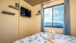 Un dormitorio con cama, televisor montado en la pared y ventana con vistas al exterior.