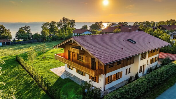 A two-story house with a balcony, surrounded by a well-maintained lawn and a view of the sea. - Suite Pfaffersee - barrier-free access with terrace and lake view (Chieming)