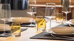 A dining table set with plates, glasses, and a bottle, with a window and curtains in the background. - Suite Pfaffersee - barrier-free access with terrace and lake view (Chieming)