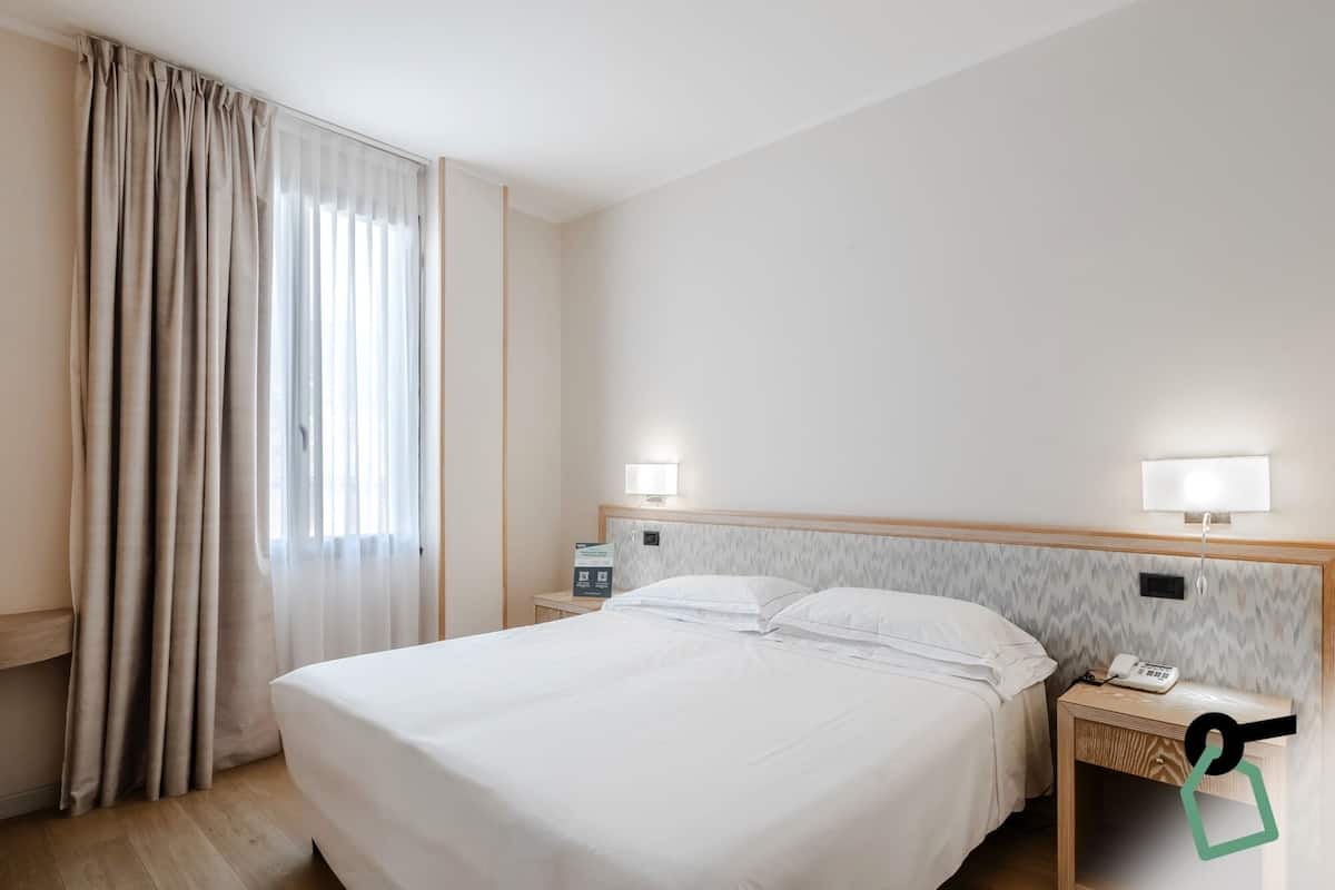 A hotel room with a large bed, two bedside tables, a telephone, and a nightstand.