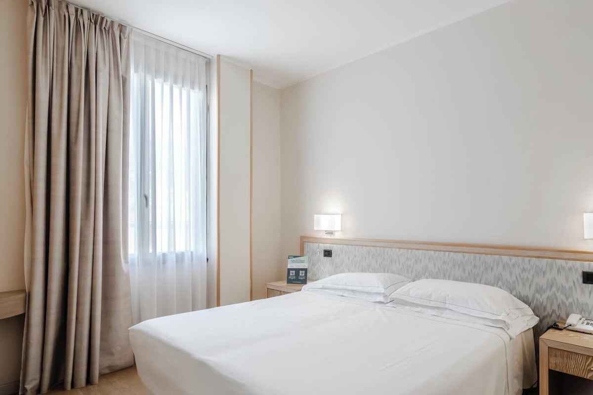A hotel room with a bed, bedside tables, a lamp, and a telephone.