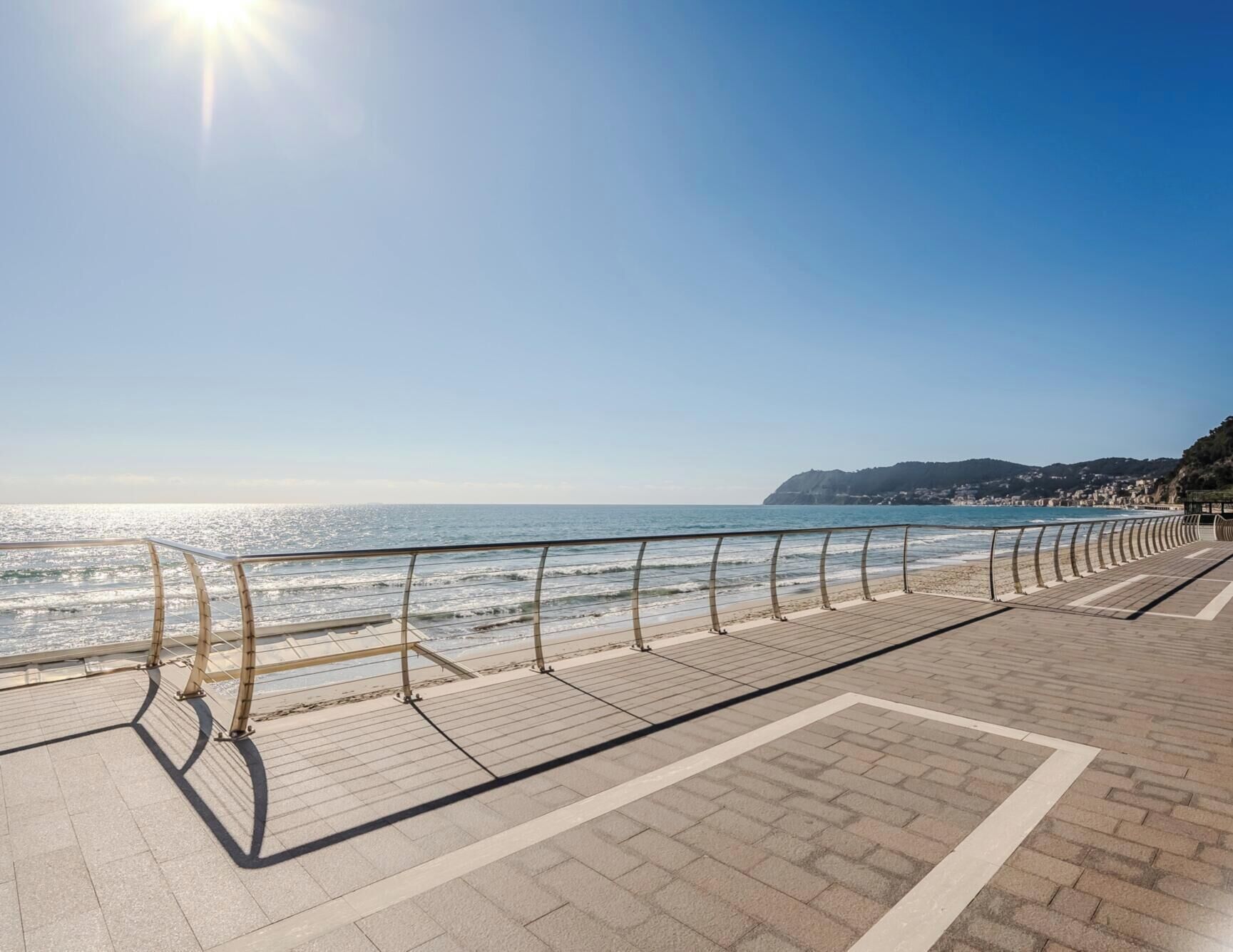 Eine gepflasterte Promenade mit Metallgeländer, die auf einen Strand blickt.
