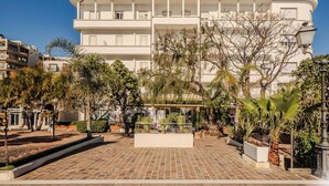 Un hotel de varios pisos con un patio central, rodeado de árboles y un paseo empedrado.