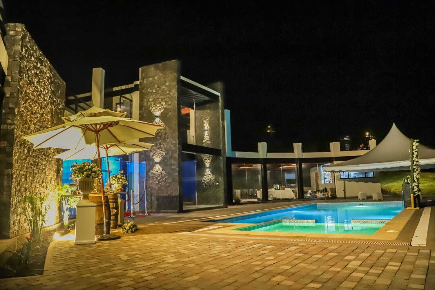 Vista nocturna de un hotel moderno con piscina, zona de estar al aire libre y un área de comedor cubierta.