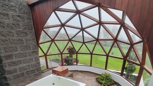 Un área de spa con hidromasaje, paredes de piedra y vistas a un campo verde a través de una ventana con marco de madera.