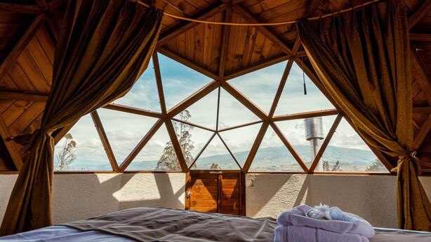 Una habitación con techo de madera, una cama con manta y vistas por una ventana.
