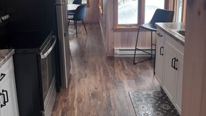 Une cuisine avec un plancher en bois, un réfrigérateur, un évier et une fenêtre donnant sur les arbres.