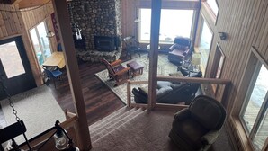 Un intérieur de chalet chaleureux avec une cheminée en pierre, des murs en bois et de grandes fenêtres.