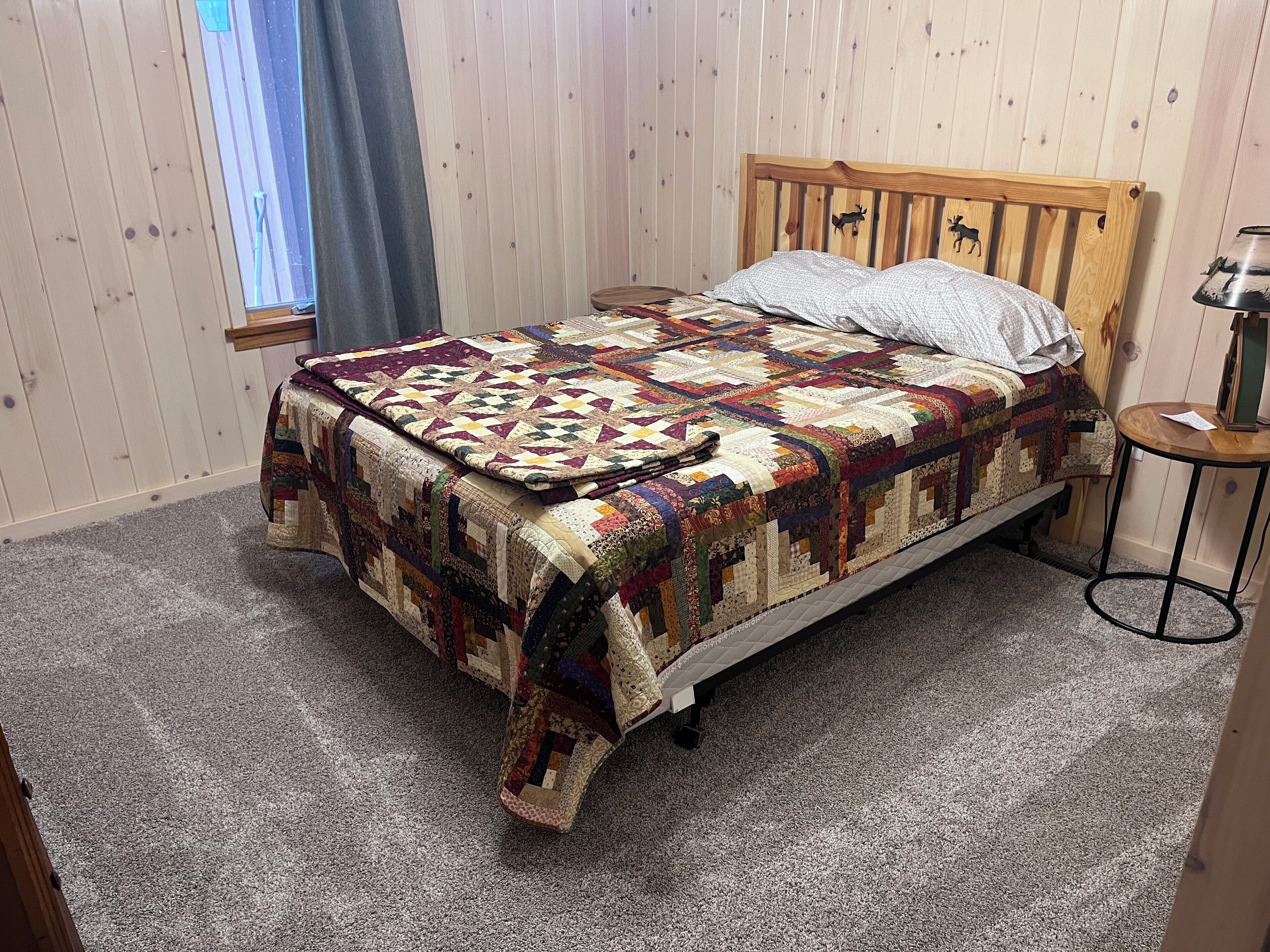 A neatly made bed with a colorful quilt, a wooden headboard with animal carvings, and a small round table with a lamp.