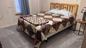 A neatly made bed with a colorful quilt, a wooden headboard with animal carvings, and a small round table with a lamp.