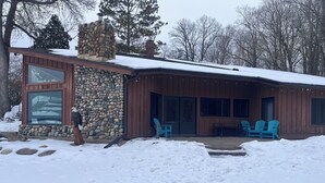 Une cabane en pierre et en bois, dotée d’une cheminée en pierre, d’une grande fenêtre et d’un patio couvert avec des chaises.