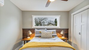 A bedroom with a bed, two bedside tables with lamps, a window with a view, and a door. - Apartment on Broadway St - K (Sugarcreek)