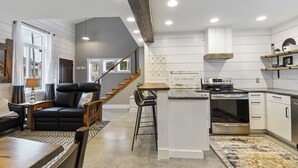 A modern kitchen with white cabinetry, a built-in oven, and a dining area with a black leather chair and a wooden table. - Apartment on Broadway St - K (Sugarcreek)