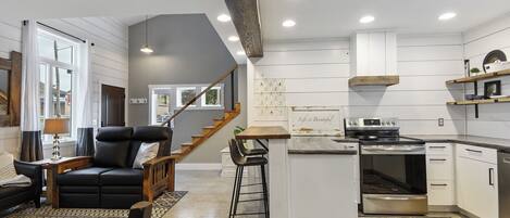A modern kitchen with white cabinetry, a built-in oven, and a dining area with a black leather chair and a wooden table.