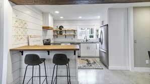 A modern kitchen with a wooden countertop, two bar stools, a refrigerator, and a view into the dining area. - Apartment on Broadway St - K (Sugarcreek)