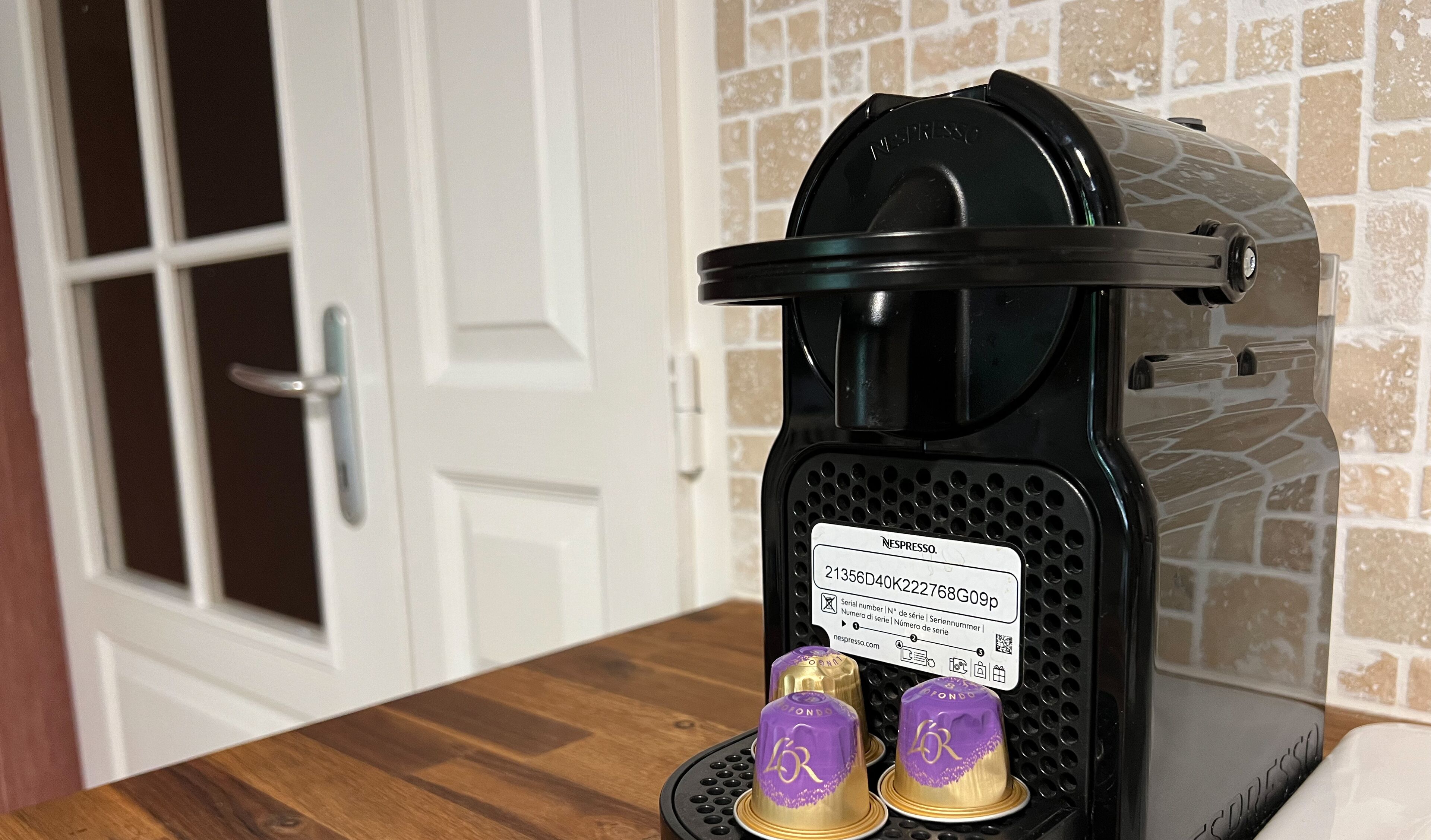 A Nespresso coffee machine with a black body and a clear water tank, placed on a wooden countertop.
