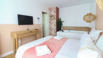 Una habitación de hotel con cama, escritorio, televisor, espejo, lavamanos y ducha.