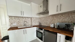 A compact kitchen with white cabinets, a tiled backsplash, a stainless steel sink, a toaster, and a dishwasher. - 123home- Garden & spa (Serris)