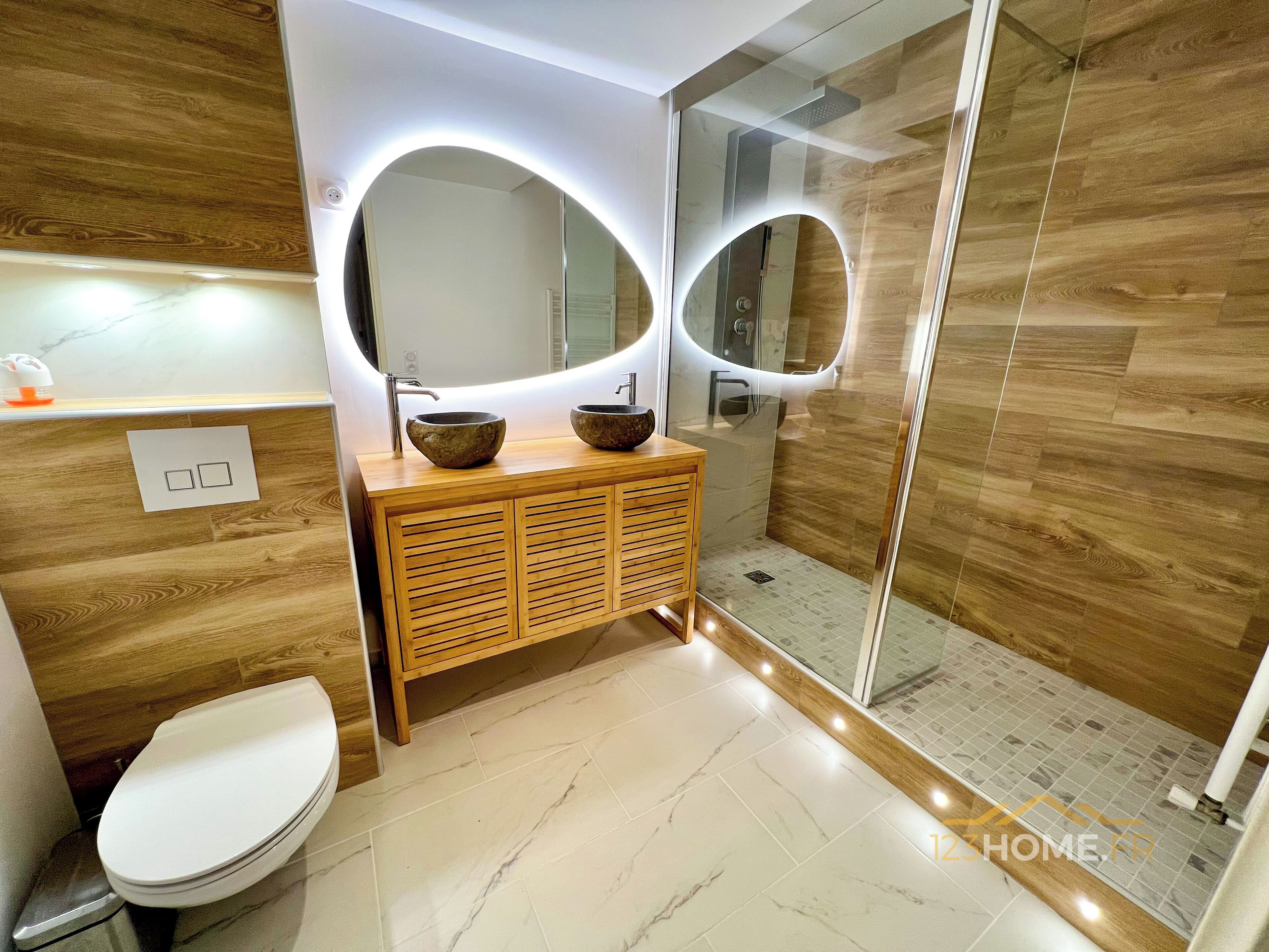 Une salle de bain moderne avec un meuble-lavabo en bois, deux vasques, un grand miroir et une douche à parois de verre.
