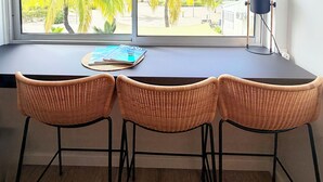 Een kamer met een groot raam, een klok, een tafel met stoelen en een lamp.