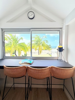 A room with a large window, a clock, a table with chairs, and a lamp.