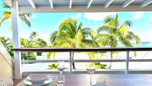 Een eettafel gedekt met borden, kommen en glazen, met uitzicht op een strand met palmbomen.
