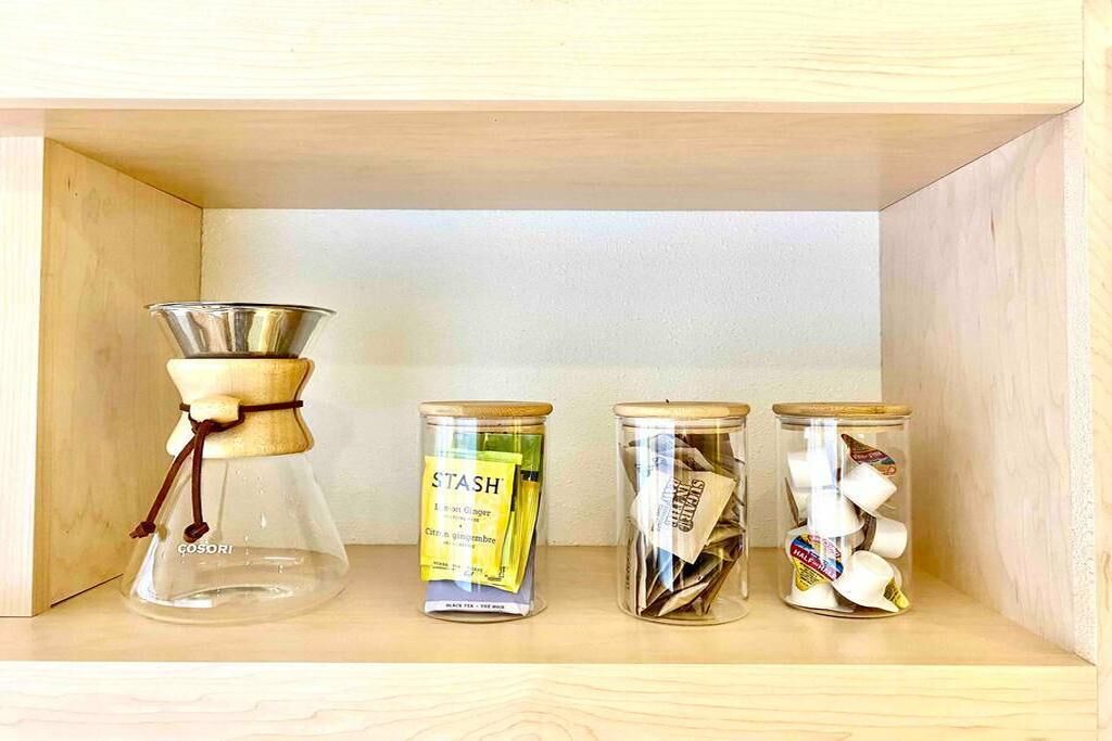 Une étagère en bois sur laquelle se trouvent une cafetière en verre, deux bocaux en verre contenant des sachets de thé et un autre bocal en verre contenant également des sachets de thé.