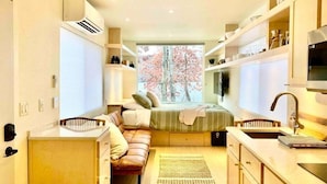 Una cocina moderna y compacta con electrodomésticos integrados, una isla central y un ventanal con vistas a los cerezos en flor.