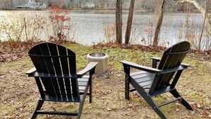 Dos sillas Adirondack mirando un lago, con una casa al fondo.