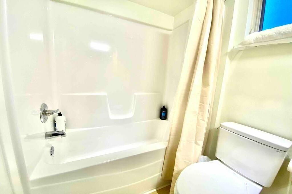 A bathroom with a bathtub, toilet, and a window with curtains.