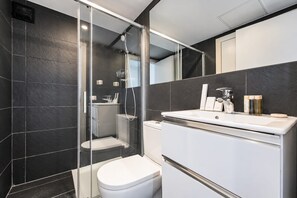 A modern bathroom with a glass-enclosed shower, a white toilet, and a vanity with a mirror.