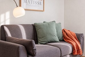 A grey sofa with a framed artwork above it, a lamp, and a blanket.