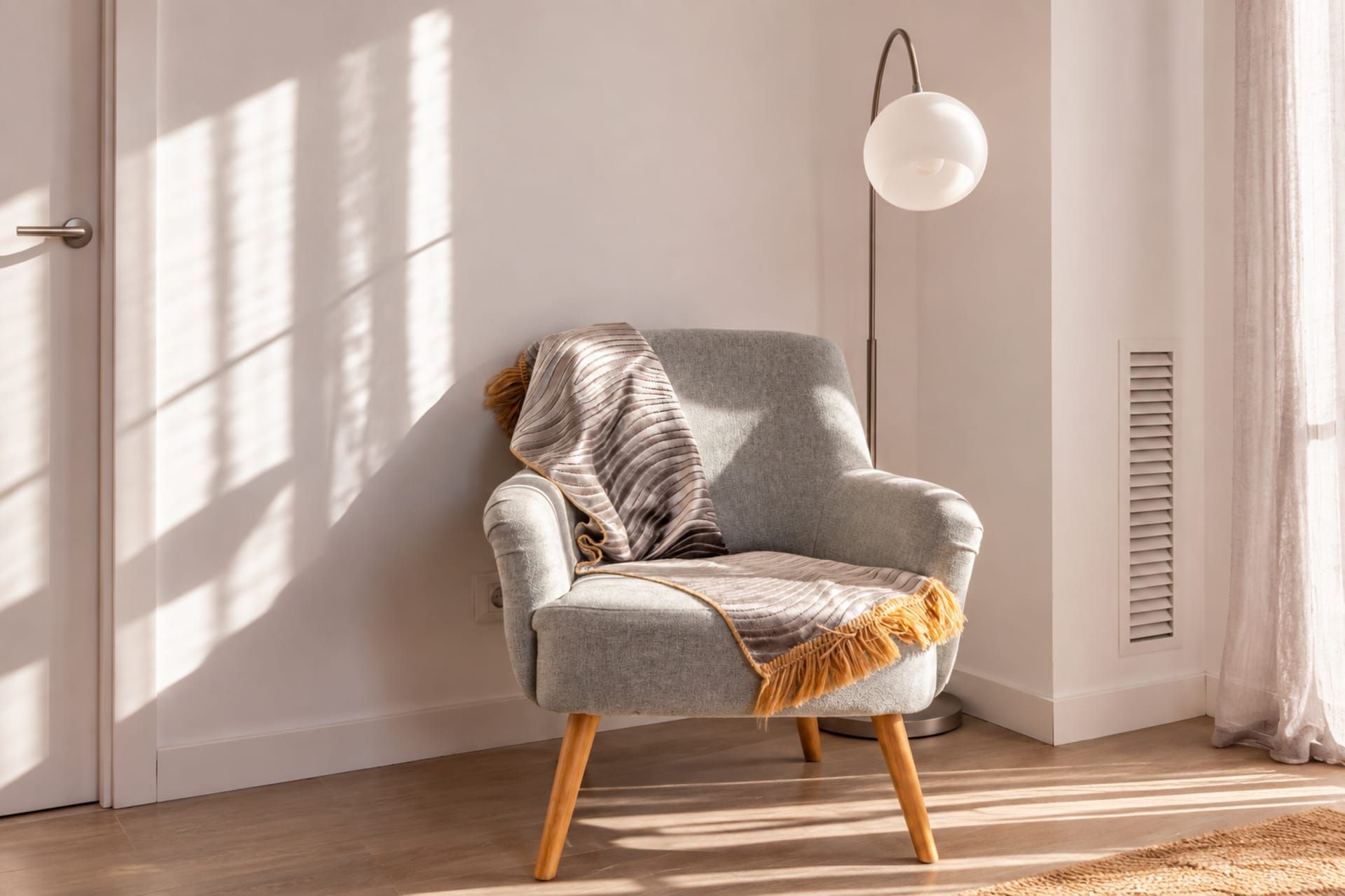 Una habitación con un sillón gris, una lámpara de pie y un ventanal con persianas.