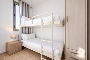 Una cama individual con mesita de noche y armario en una habitación con ventana y cortinas.