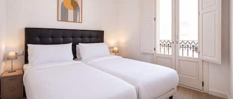 A double bed with a dark headboard, two bedside tables with lamps, a framed picture on the wall, and a balcony with a metal railing.