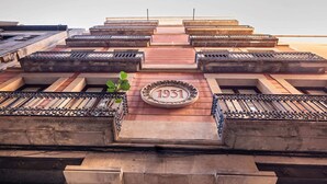 Un edificio con una placa destacada que dice '1931', varios balcones con barandillas de metal y una entrada central con escalones.