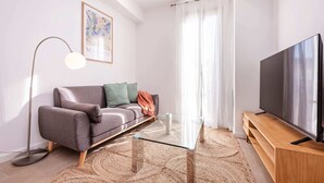 A modern living room with a grey sofa, a glass coffee table, a floor lamp, a flat-screen TV, and a wooden TV stand. - Sweett | Symphonic Central 401 (Barcelona)
