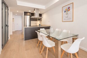 Een moderne keuken met een centraal eiland, witte stoelen en een glazen eettafel.