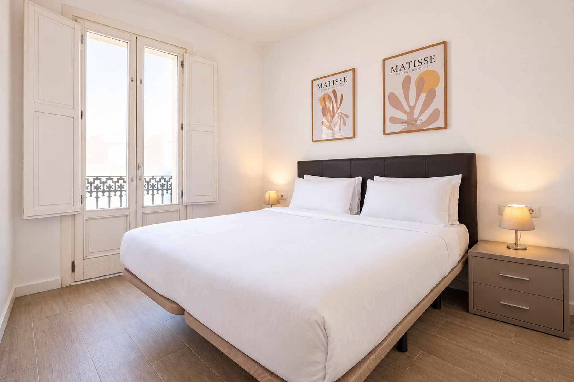 A hotel room with a large bed, two bedside tables, a window with shutters, and two wall-mounted artworks.