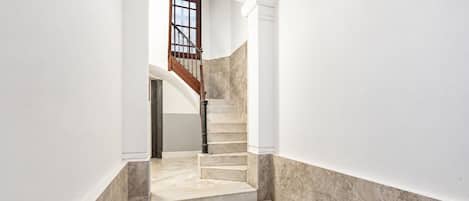 Una escalera de mármol conduce a una plataforma, flanqueada por paredes blancas y una puerta de madera.