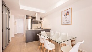 Uma cozinha moderna com uma ilha central, cadeiras brancas em torno de uma mesa de vidro e uma obra de arte emoldurada na parede.