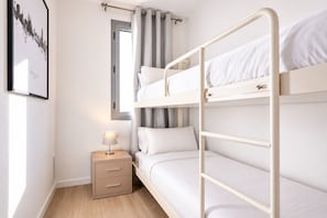 A bunk bed with a bedside table and a lamp, a window with curtains, and a framed picture on the wall.