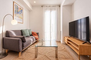 A modern living room with a sofa, a glass coffee table, a TV on a wooden stand, and a floor lamp.